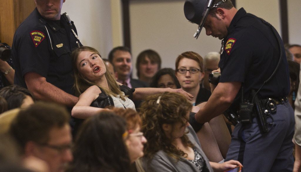 A woman protesting Gov. Scott Walker's Act 10 collective bargaining reform law was removed from a meeting of the Legislature's Joint Committee on Finance at the Wisconsin state Capitol in June 2011. Walker says the law has saved taxpayers $3 billion.