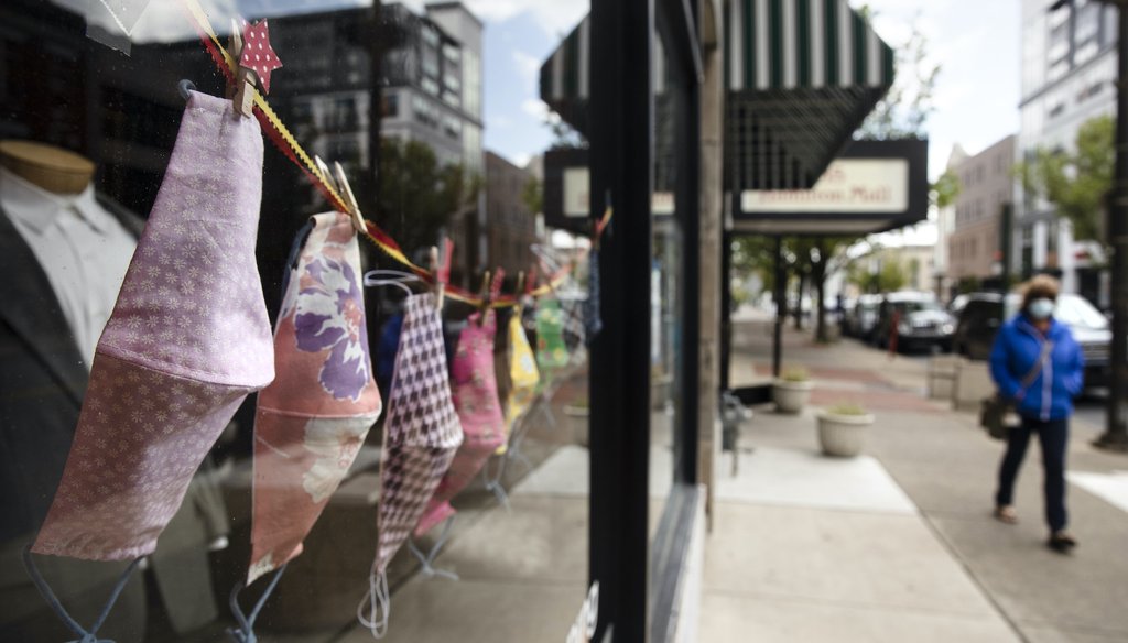 A person wearing a protective face mask as a precaution against the coronavirus walks by a shop displaying face coverings in Allentown, Pa., Tuesday, May 12, 2020. (AP Photo/Matt Rourke)